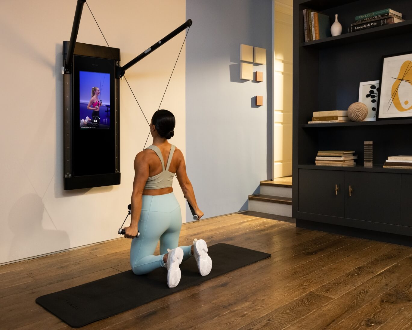A woman is working out in her living room. She is facing Tonal and is completing an X-Pulldown Tricep Extension.