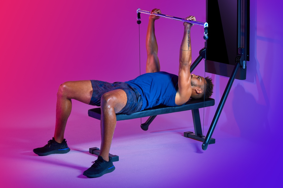 A man lies back on a bench and works on his bench press with Tonal — discover how to improve your bench press with data