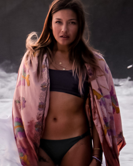 Coach Nikki wearing a black two-piece swimsuit and a pink pareo on a beach
