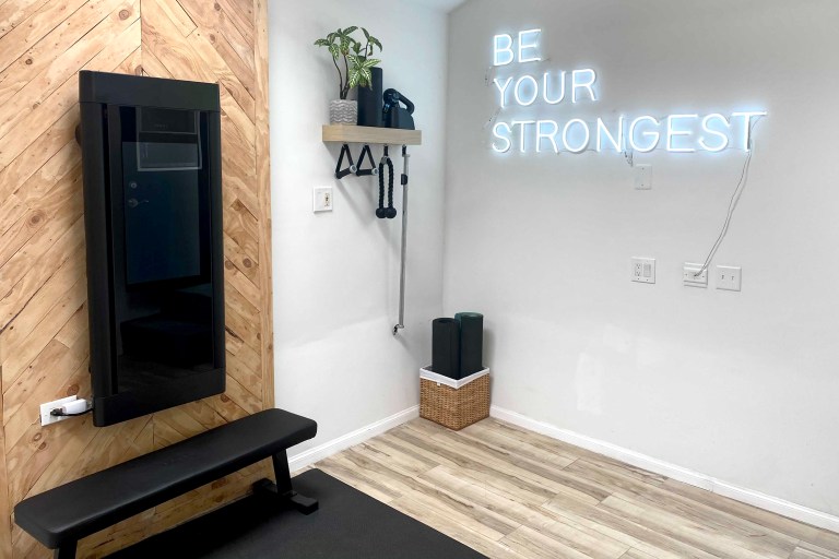 Tonal home gym with Be Your Strongest neon sign