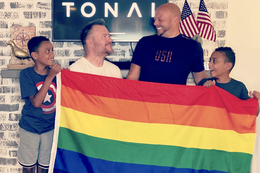 two men hold up the Pride flag with their twin sons 