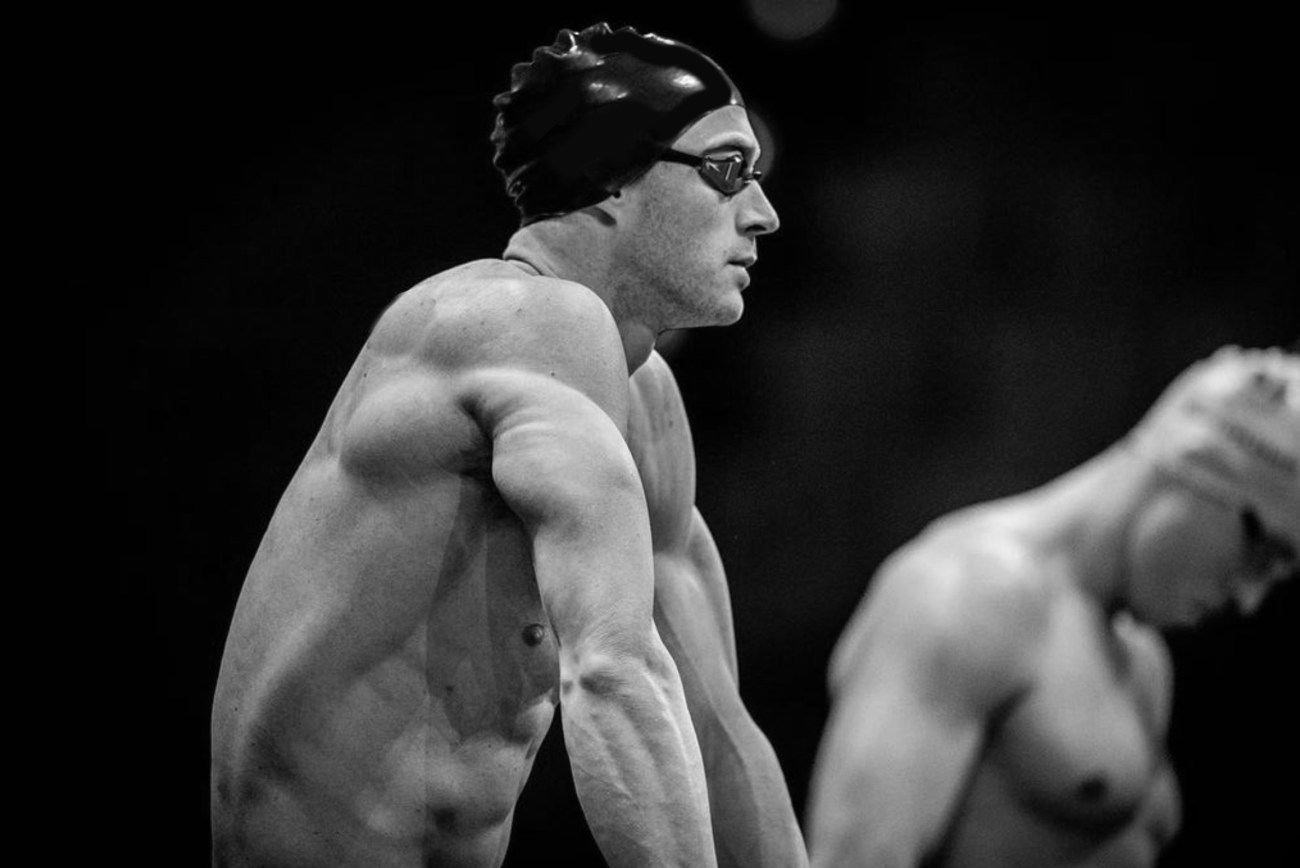 black and white image of a male swimmer wearing a hat and goggles