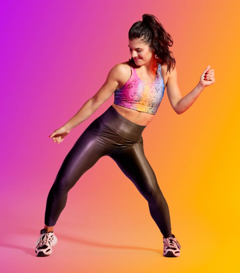 A woman in workout clothes dances against a multi-colored backdrop.