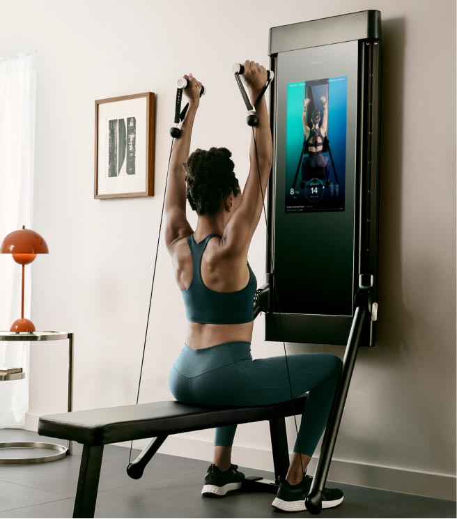 A woman performs an overhead press using her Tonal smart home gym machine.