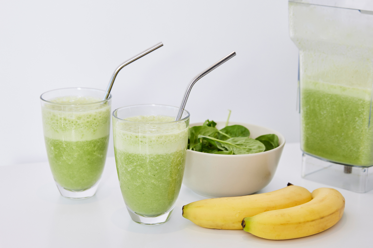 two glasses of green protein smoothie and bananas lying next to it