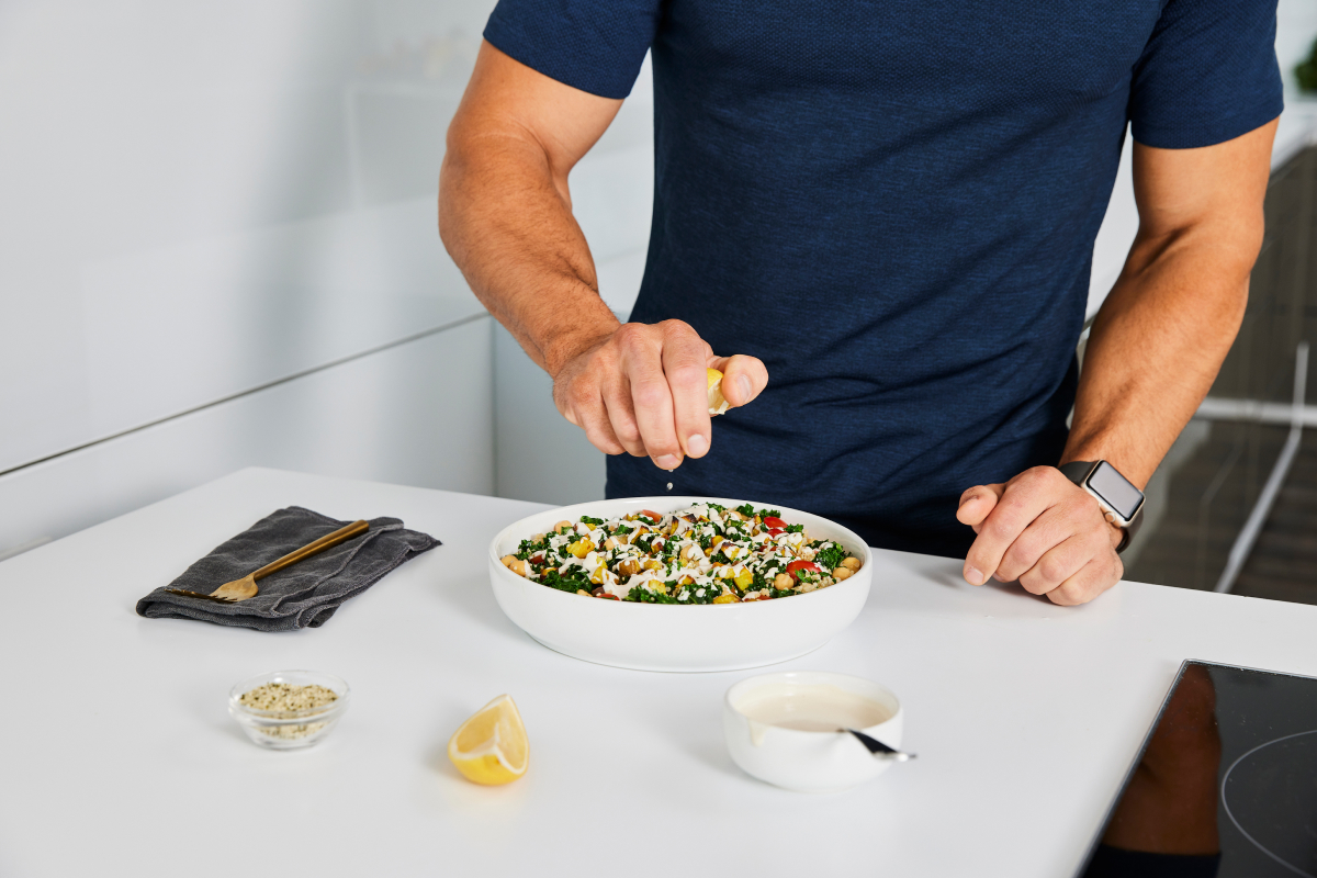 a man squeezing lemon juice over a bowl of kale and chickpeas demonstrating a healthy grain bowl recipe