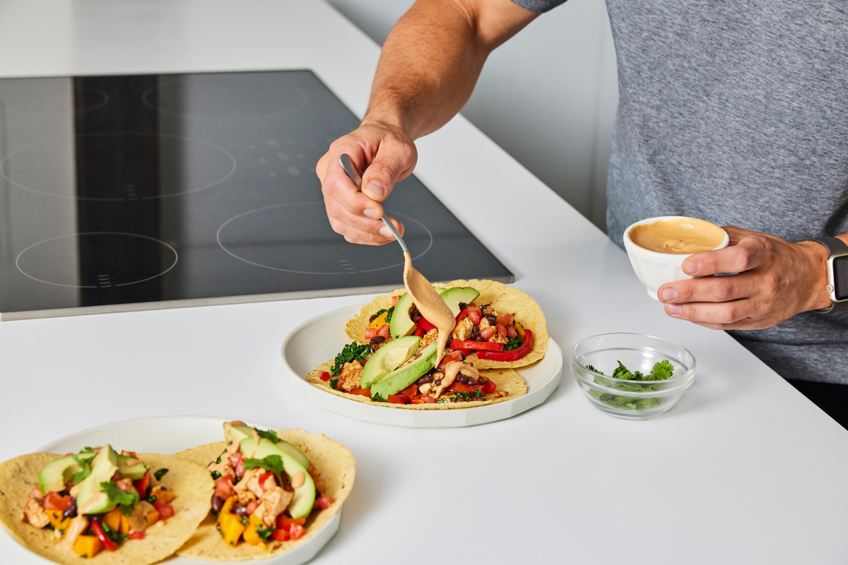 image of a man drizzling crema onto a tacos loaded with colorful vegetables and avocado 