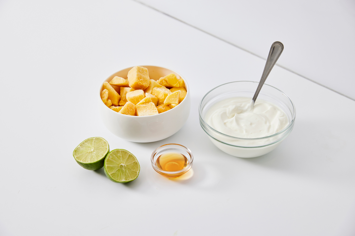 frozen mango, yogurt, a lime and some honey in bowls to demonstrate a frozen yogurt recipe