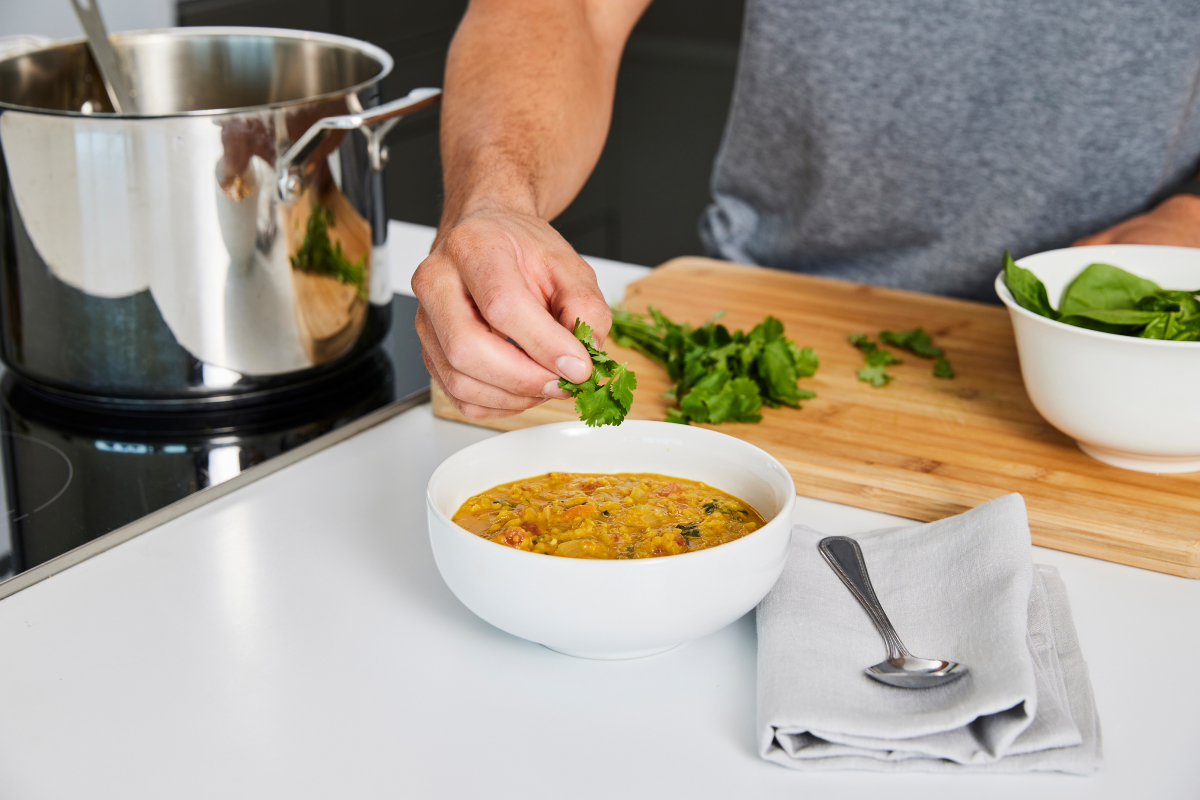 a man garnishing a bowl of red lentil dal with some cilantro 