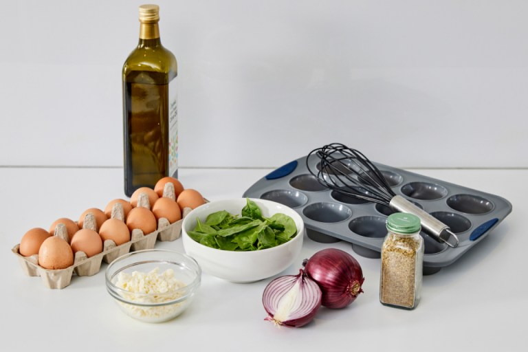 a counter with a collection of ingredients: eggs, spinach, and onion