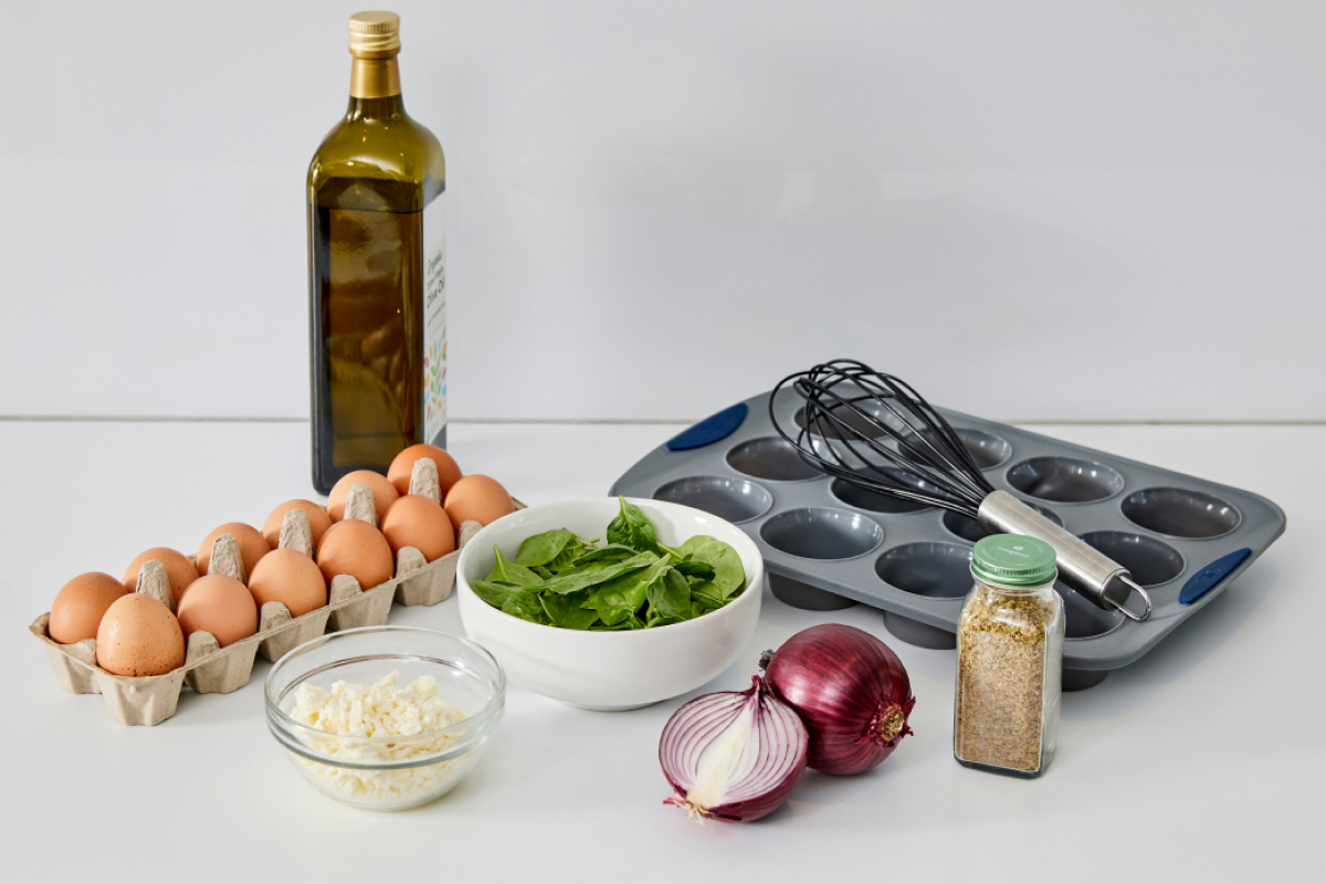Image of ingredients on a counter: eggs, spinach, onion, and feta and kitchen utensils demonstrating a healthy eating habits