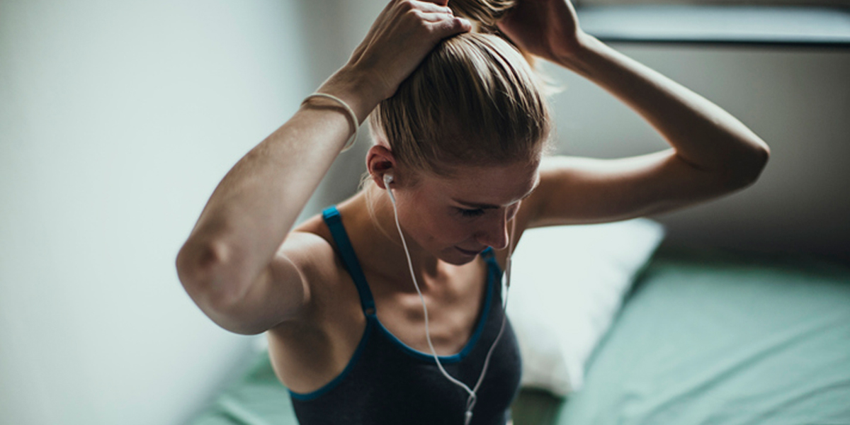 How to start exercising again. Woman in workout clothes and headphones tying her hair into a ponytail.
