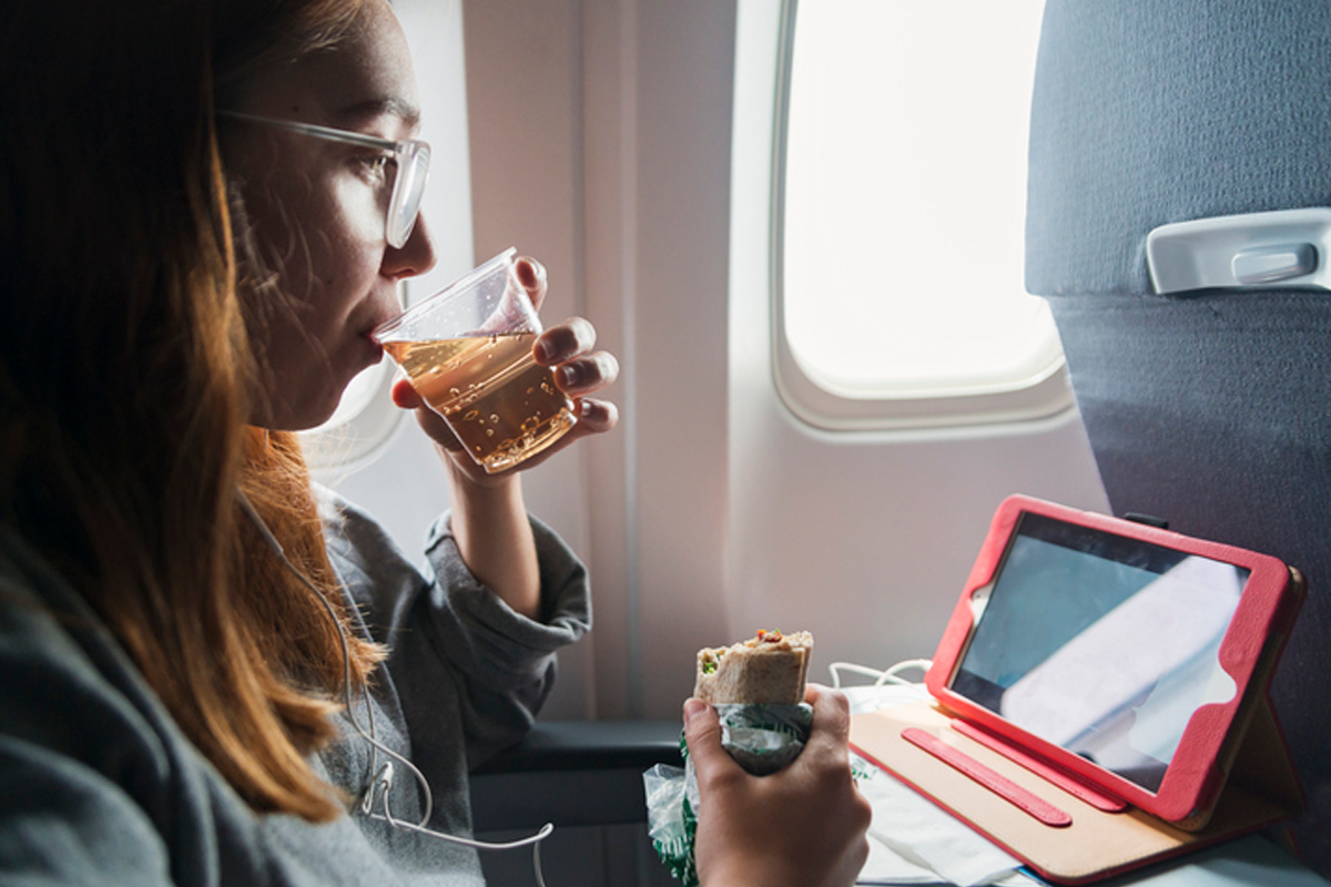 Woman on an airplane eating a wrap and drinking a ginger ale. 
