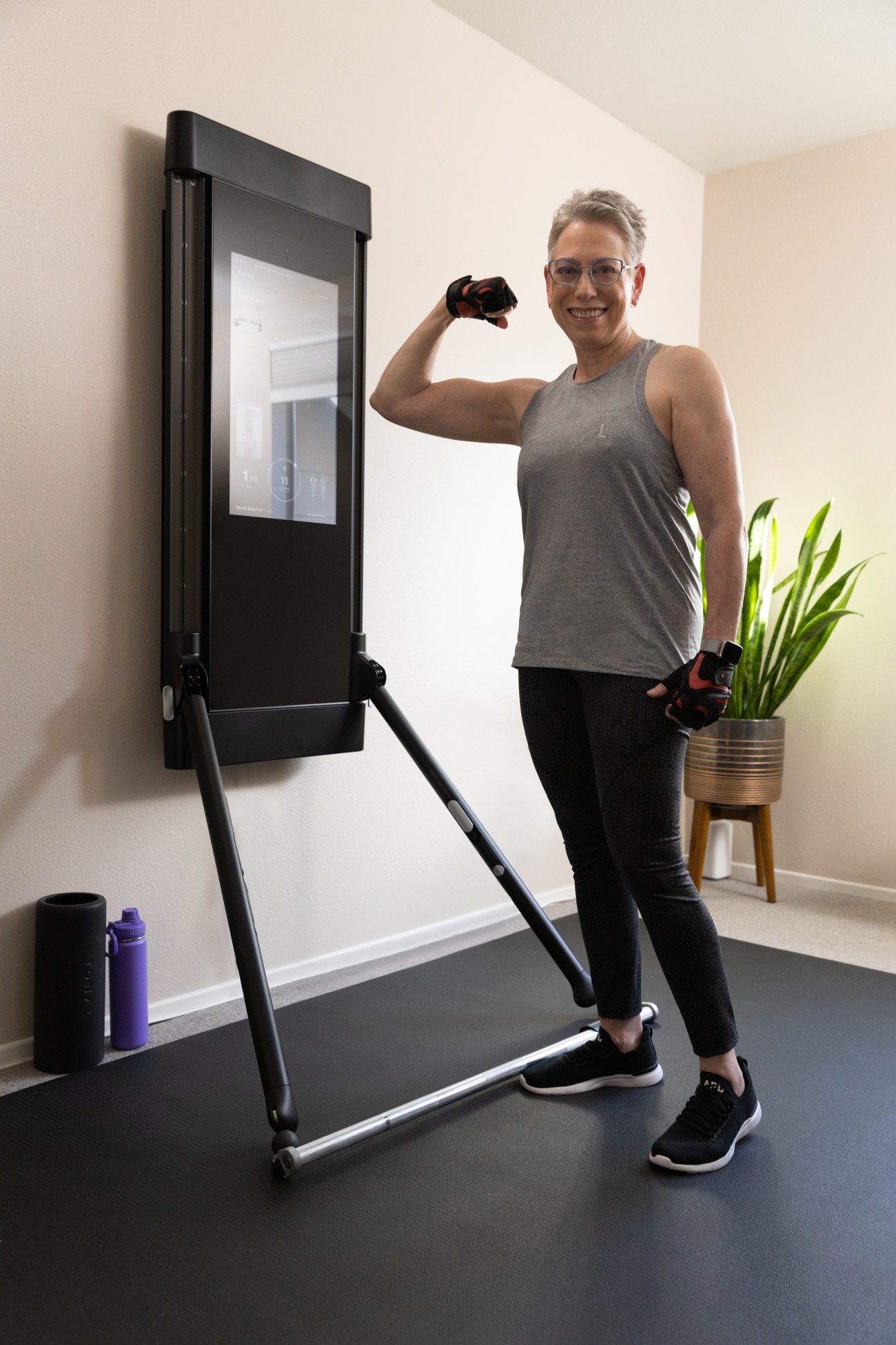 Arlene Kraushaar flexing her bicep in front of Tonal in her home gym.