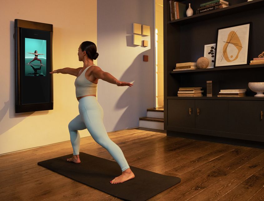 A woman is working out in her living room. She is following a Yoga workout on Tonal.