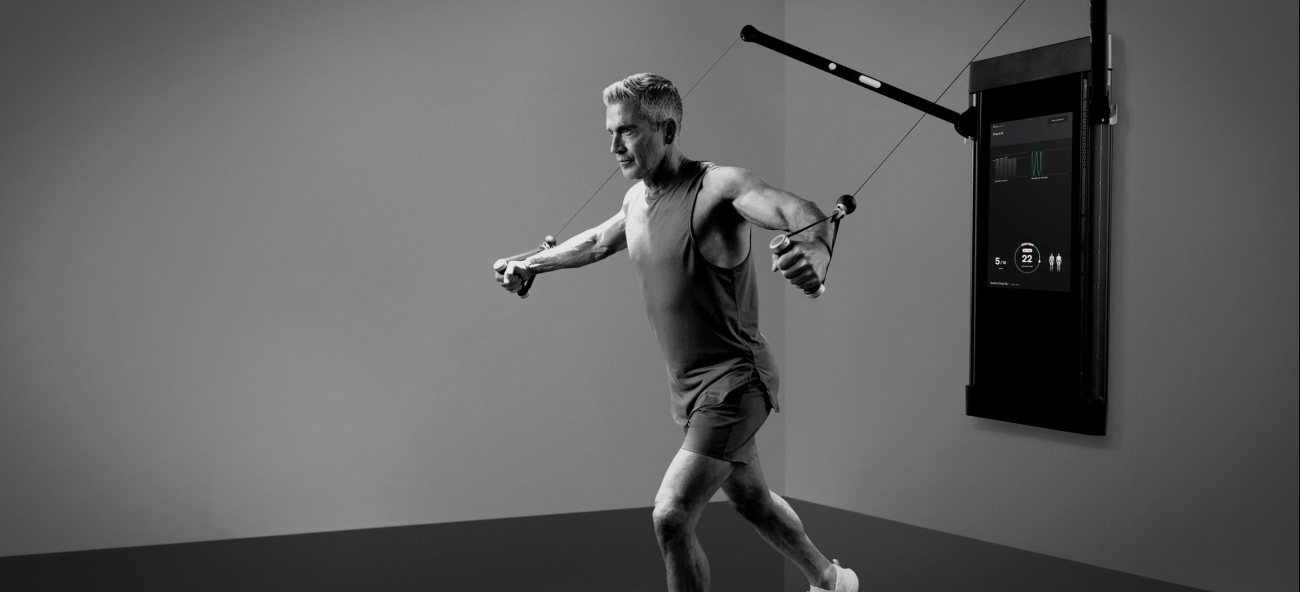 A man stands with his back facing the Tonal while grabbing both cables to perform a chest fly exercise.