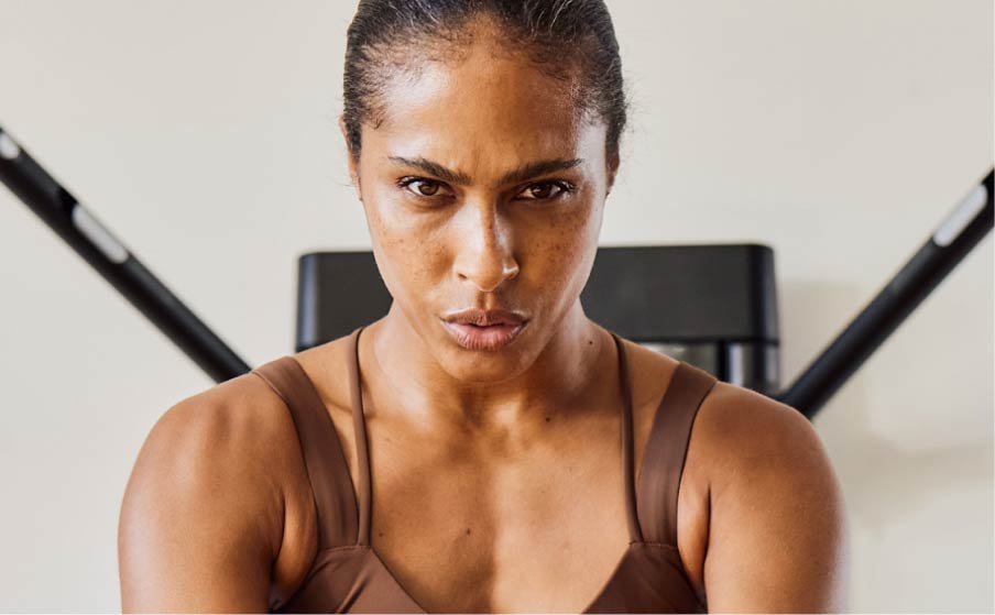 A woman stands with her back facing the Tonal, the shot centered on her face as she works out. 