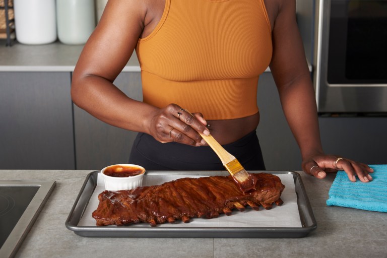 Coach Tanysha Renee brushing BBQ pork ribs with low-sugar BBQ sauce.